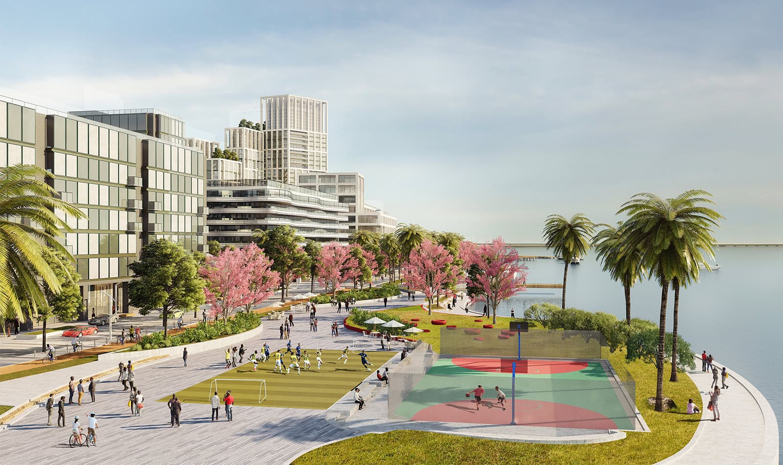 The lagoon-edge promenade at Paradise Wharf, a five-a-side pitch and a basketball court beside the water under palms and blossom trees